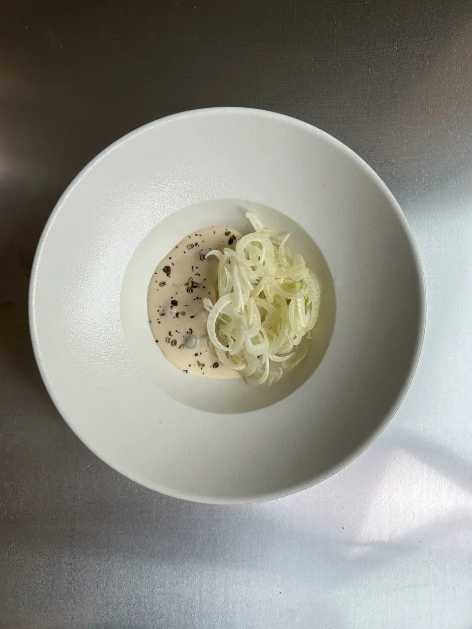 Tynde fennikelstrimler og en cremet sauce med knust peber i en hvid dyb tallerken