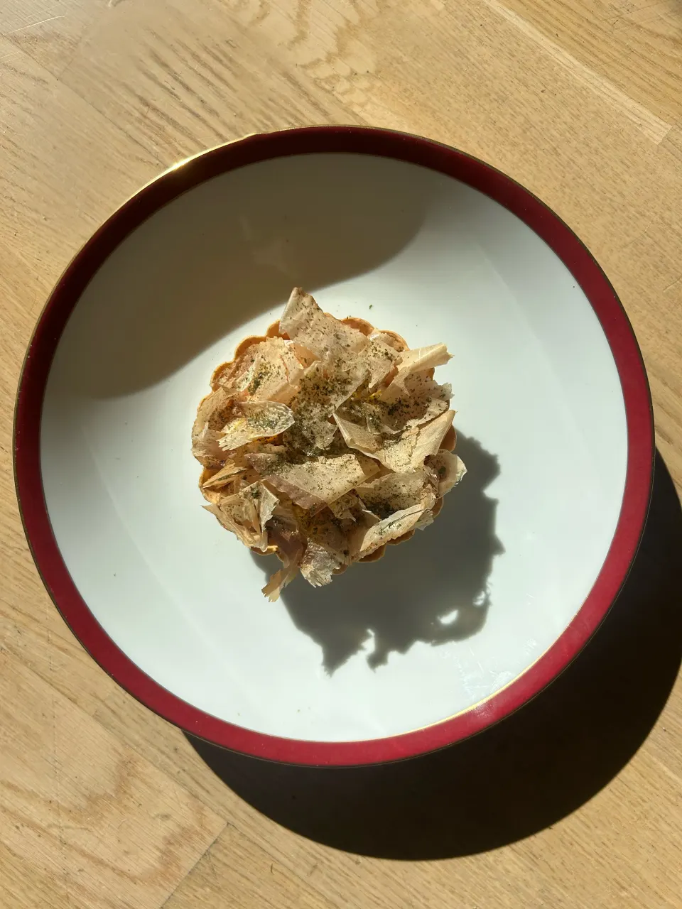 Fransk-japansk tartelet toppet med katsuobushi og aonori på en hvid tallerken med rød kant